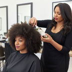 Professional stylist applying natural hair styling products to a client with thick afro-textured hair, showcasing hair care products for black hair.